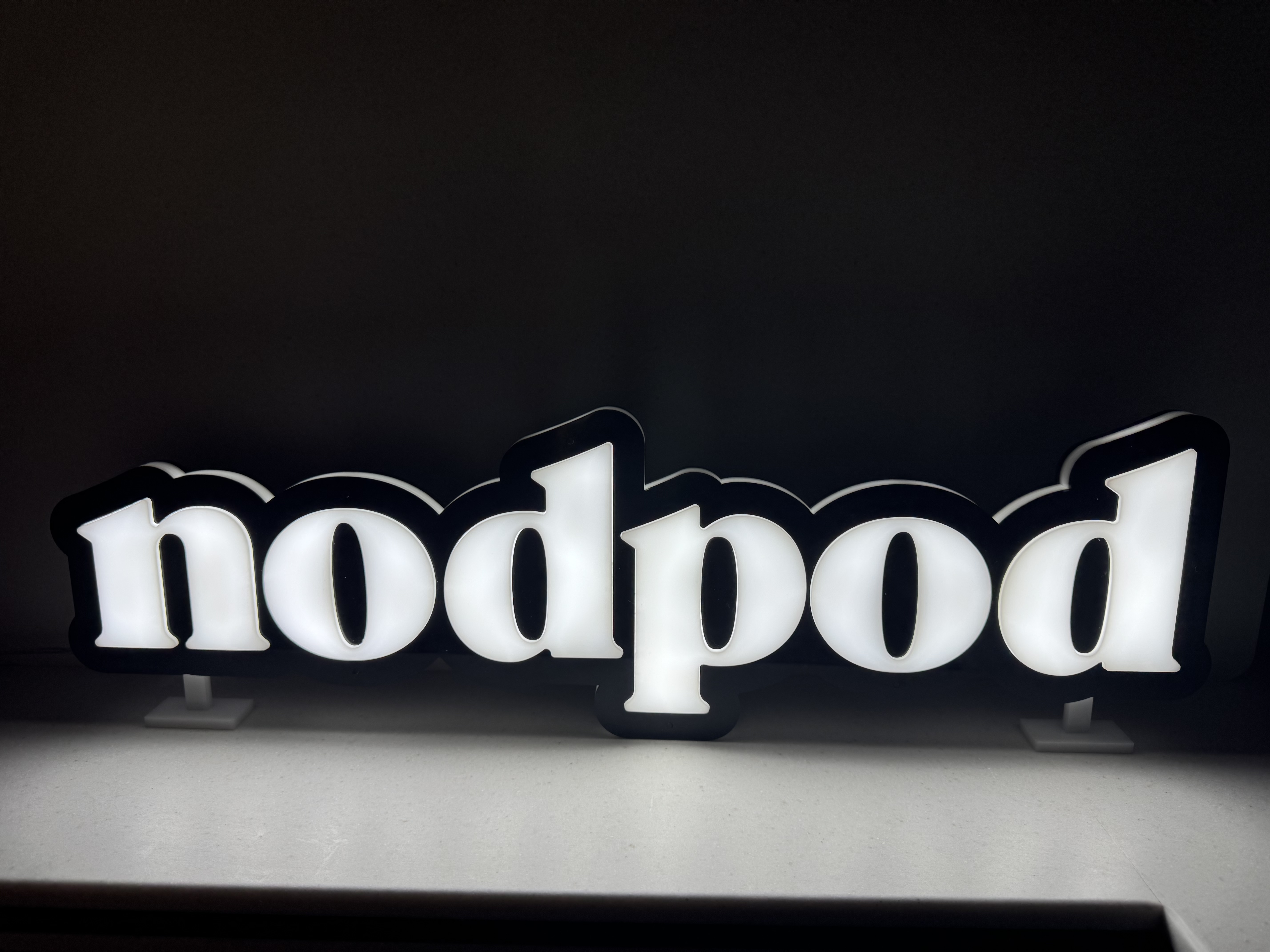 White illuminated nodpod acrylic lettering with a black outline